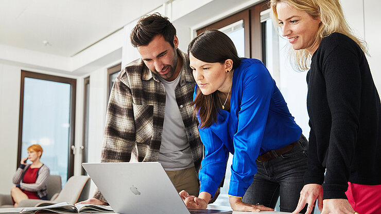Drei Menschen schauen auf ein Laptop